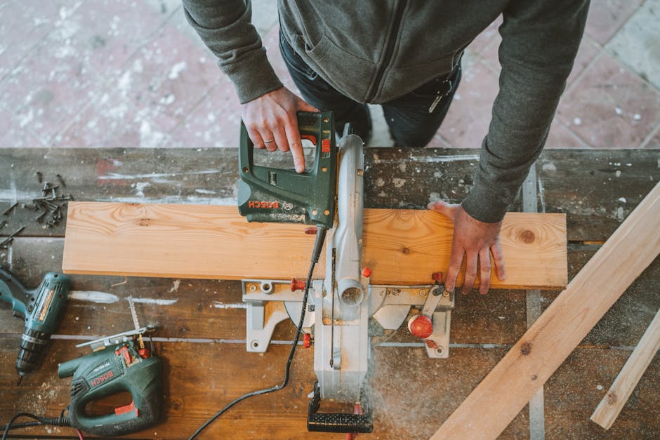 A woodworker operates an electric jigsaw on a wooden plank, surrounded by tools.