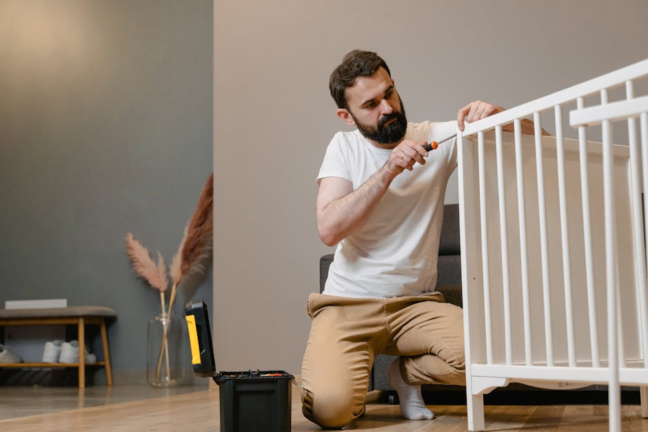 Father kneels to fix a white baby crib using a screwdriver in a contemporary nursery setting.